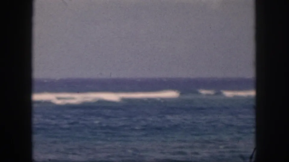 1959 Hawaii home-movie view of rolling blue water and white foam bands, partially blocked by dark vertical framing.