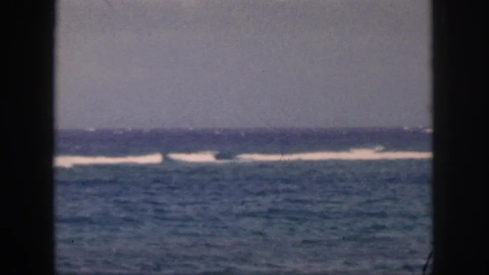1959 Hawaii 8mm frame showing a blue ocean horizon, white surf breaks, gray sky, and dark window-frame edges.