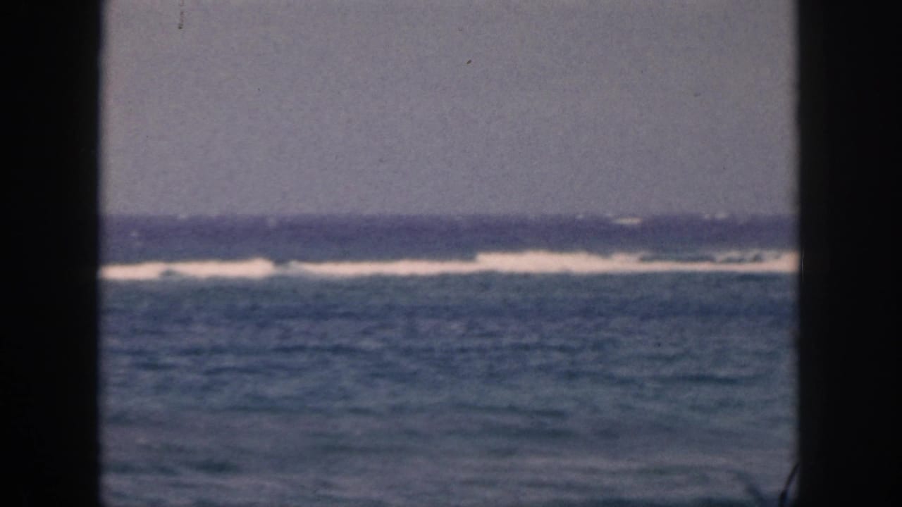 1959 Hawaii 8mm home-movie frame showing distant surf and open ocean viewed through dark window or porch framing.