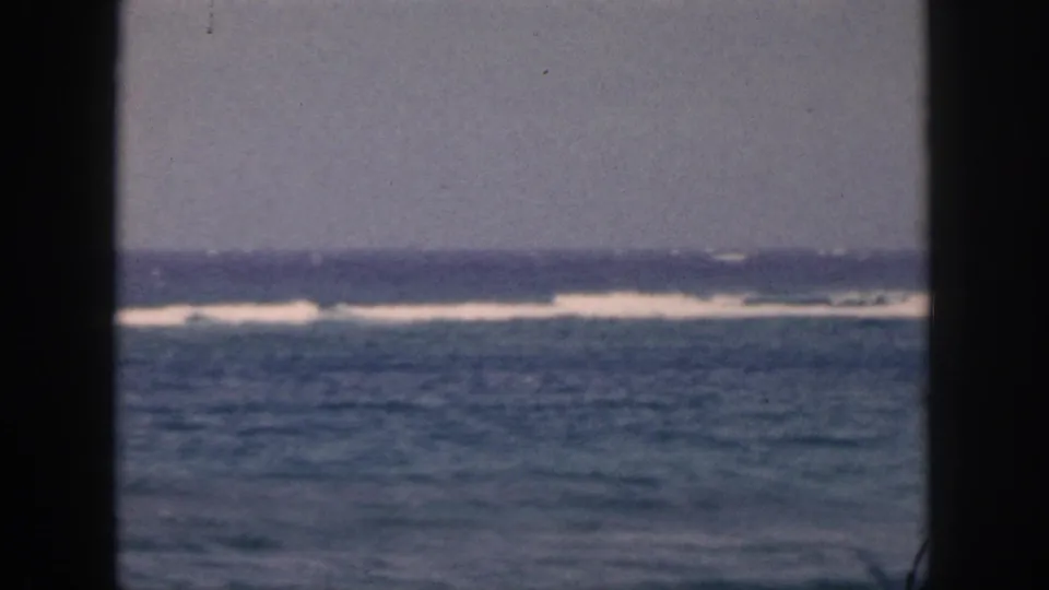 1959 Hawaii 8mm home-movie frame showing distant surf and open ocean viewed through dark window or porch framing.