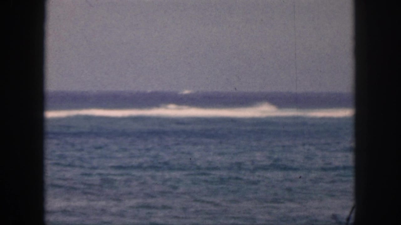 1959 Hawaii coastal view with white surf breaking in the distance, framed by dark vertical bars in an 8mm home-movie shot.