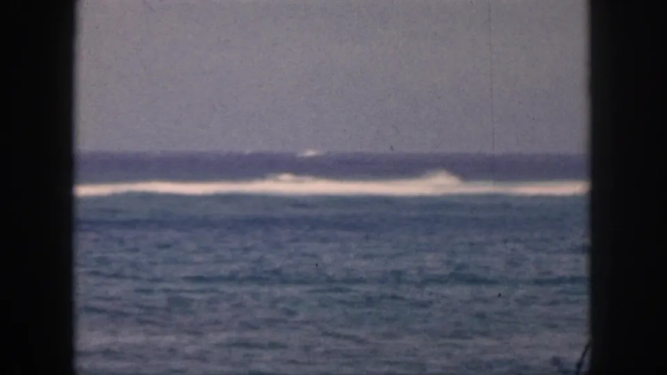 1959 Hawaii coastal view with white surf breaking in the distance, framed by dark vertical bars in an 8mm home-movie shot.