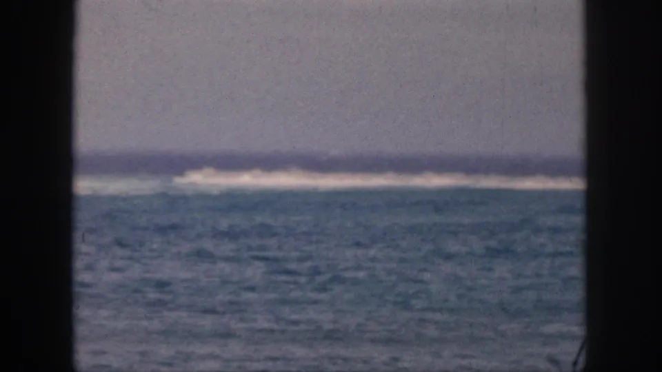 1959 Hawaii home-movie still of open water and a distant surf band, partially blocked by dark window or porch framing.