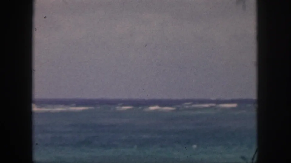 1959 Hawaii coastal view with distant white surf, muted blue water, and a dark central divider from the shooting position.