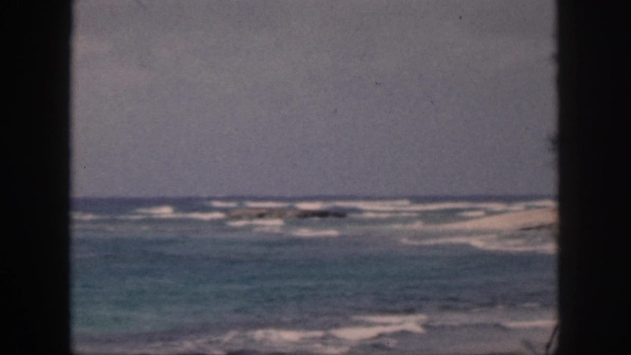 1959 Hawaii home-movie frame with blue-green water, breaking white waves, and a dark central window bar dividing the view.