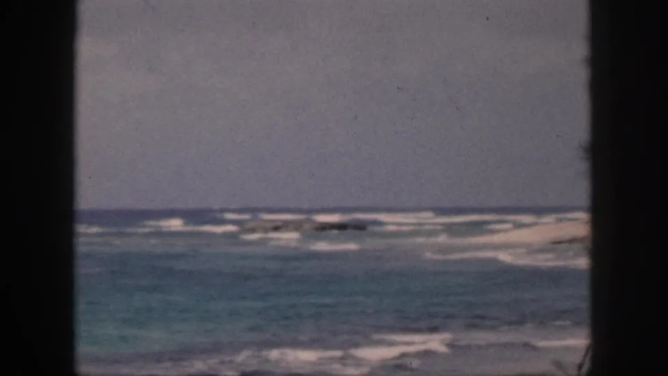1959 Hawaii home-movie frame with blue-green water, breaking white waves, and a dark central window bar dividing the view.