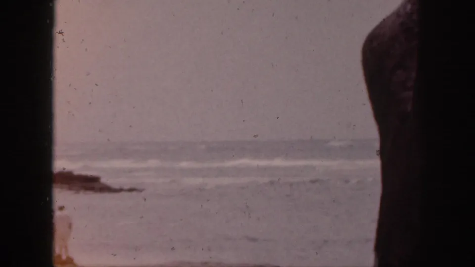 1959 Hawaii shoreline frame with ocean waves, beach, and a dark vertical obstruction at center.