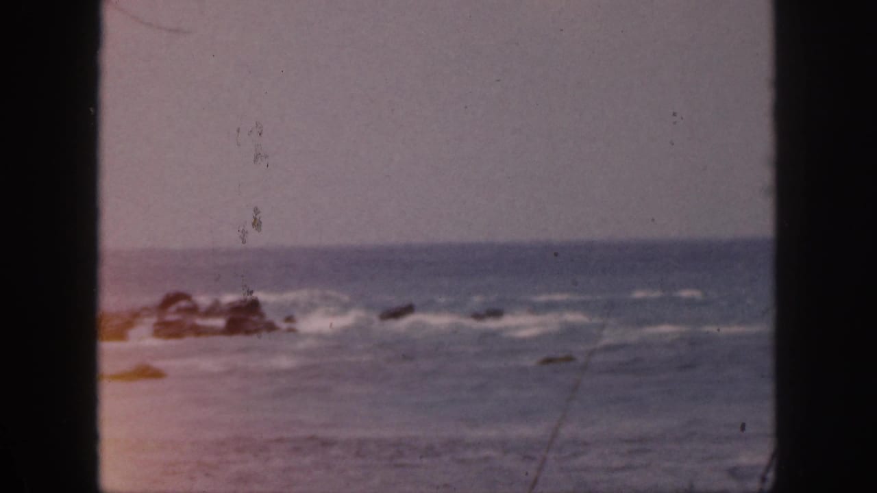 Blue-gray ocean with white surf breaking around scattered dark rocks.