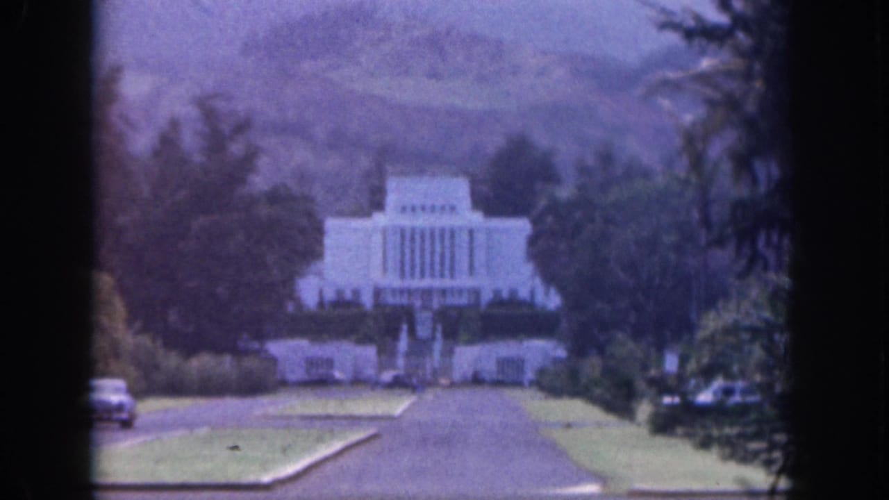 1959 Hawaii 8mm frame showing a distant white temple-like building at the end of a landscaped road with trees and hills behind it.