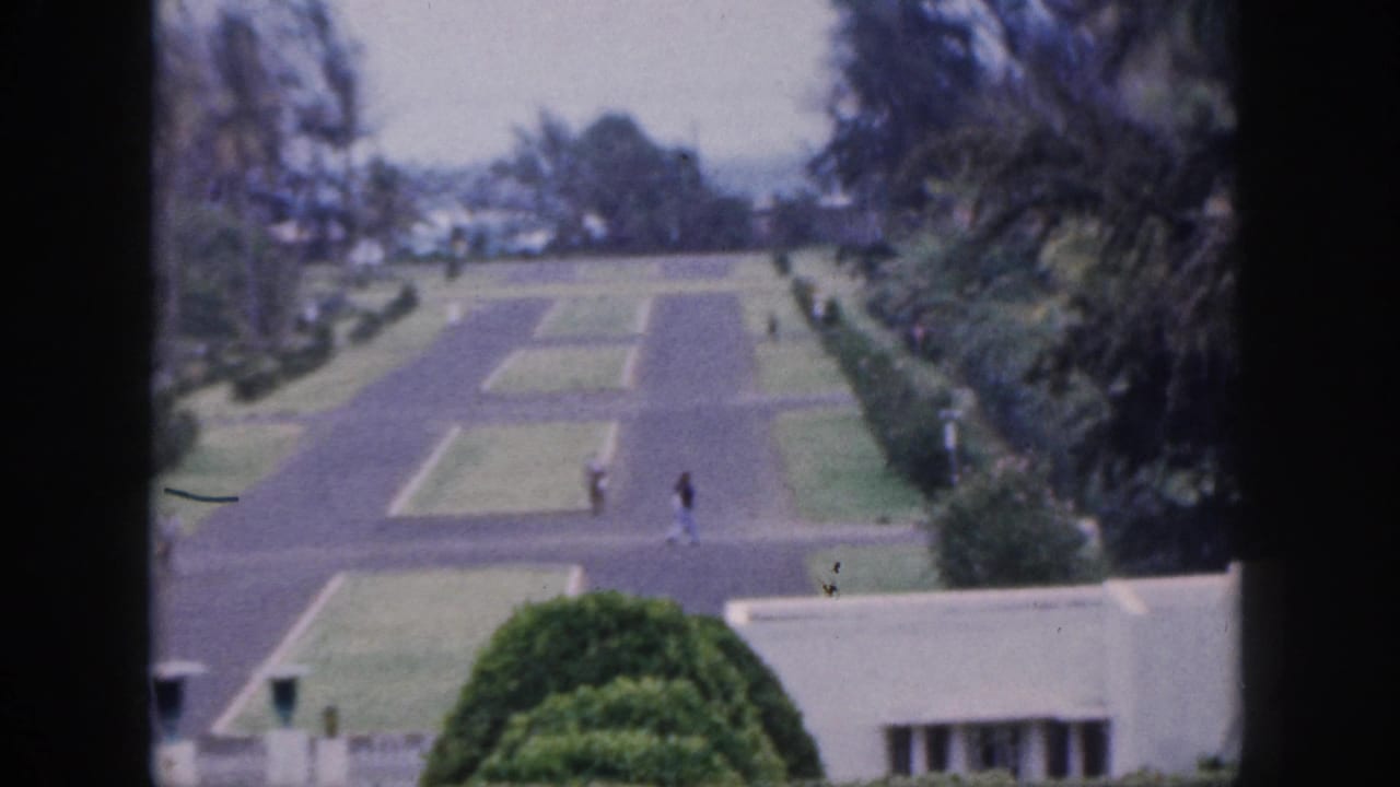 Landscaped paved path with lawns, dense trees, a low wall, and two distant walkers.