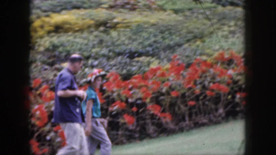 The couple continues through the garden, framed by red flowers and greenery in a vintage Hawaii travel scene.