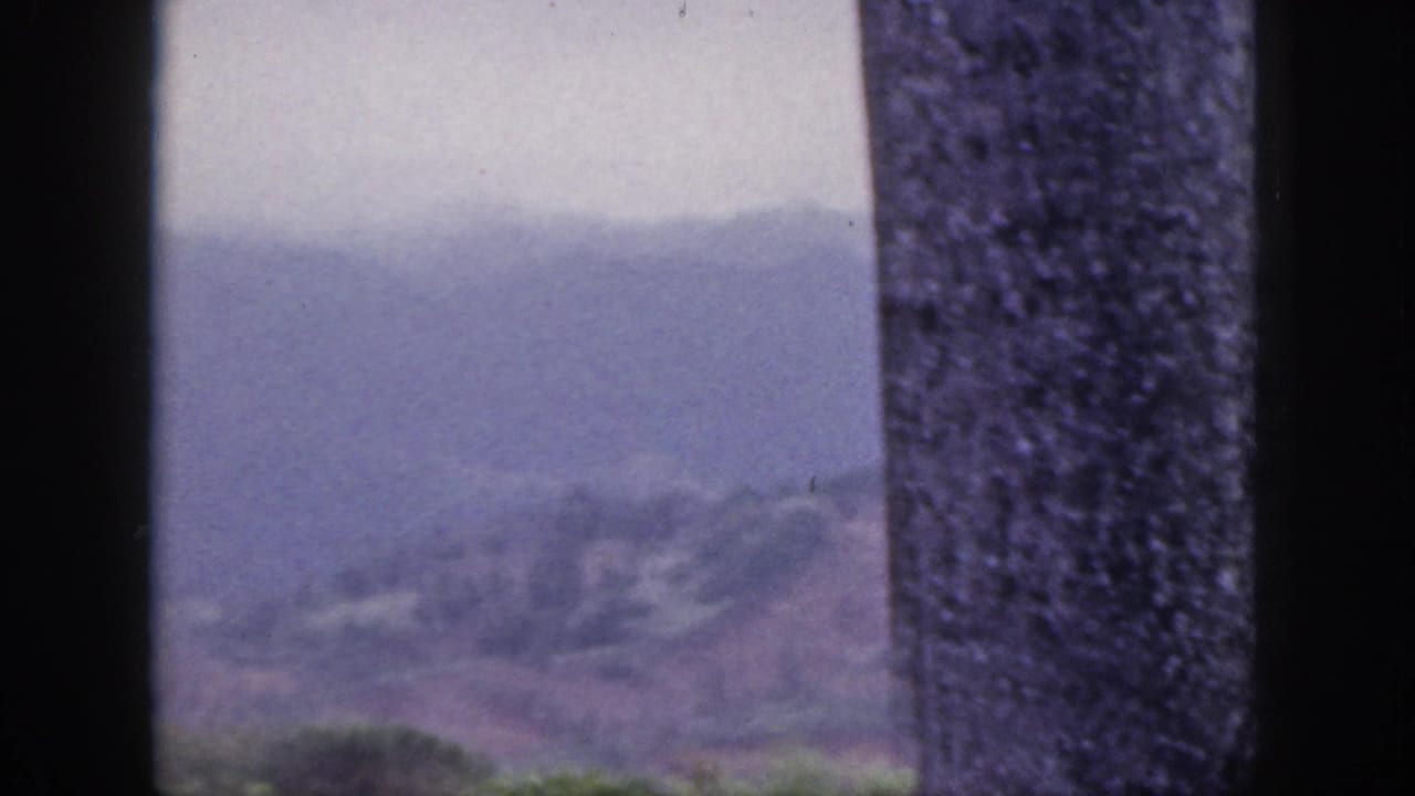 1959 Hawaii 8mm frame showing hazy mountain ridges through a dark window frame with a textured pillar in the foreground.