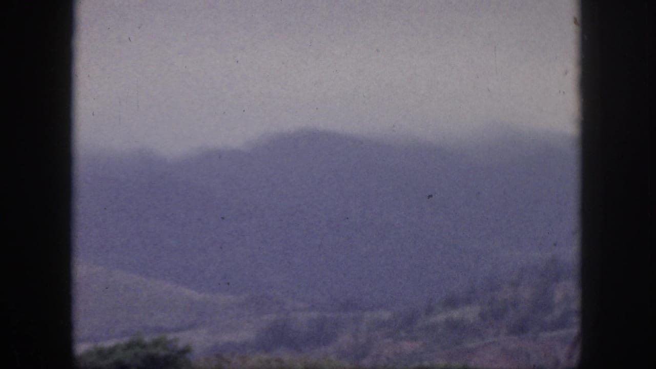 Hazy mountain ridges viewed through a dark vertical window frame.