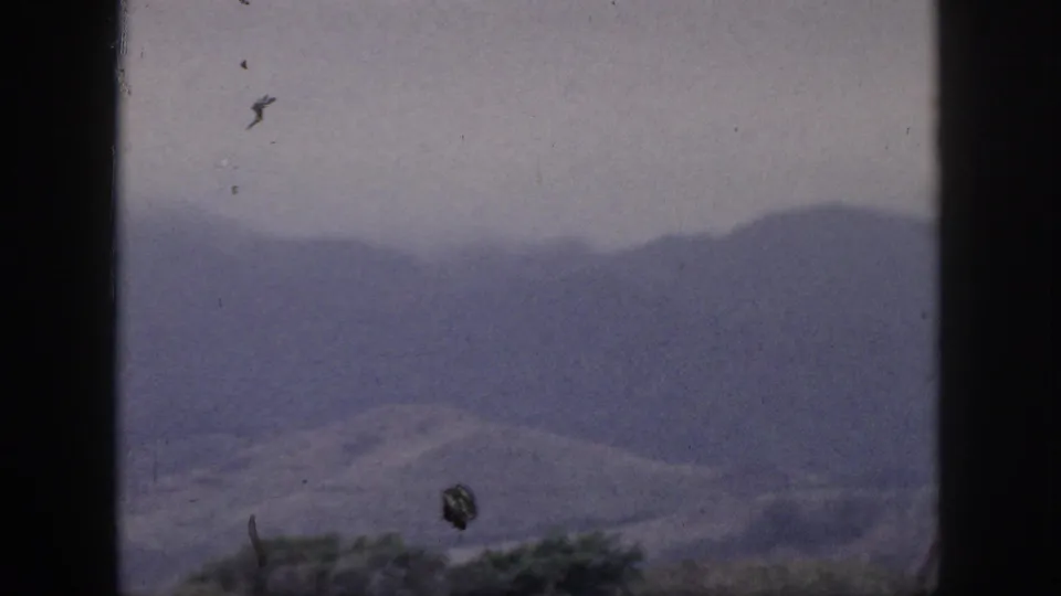 1959 Hawaii 8mm still showing a subdued mountain slope through dark window framing, with dust marks and soft focus.
