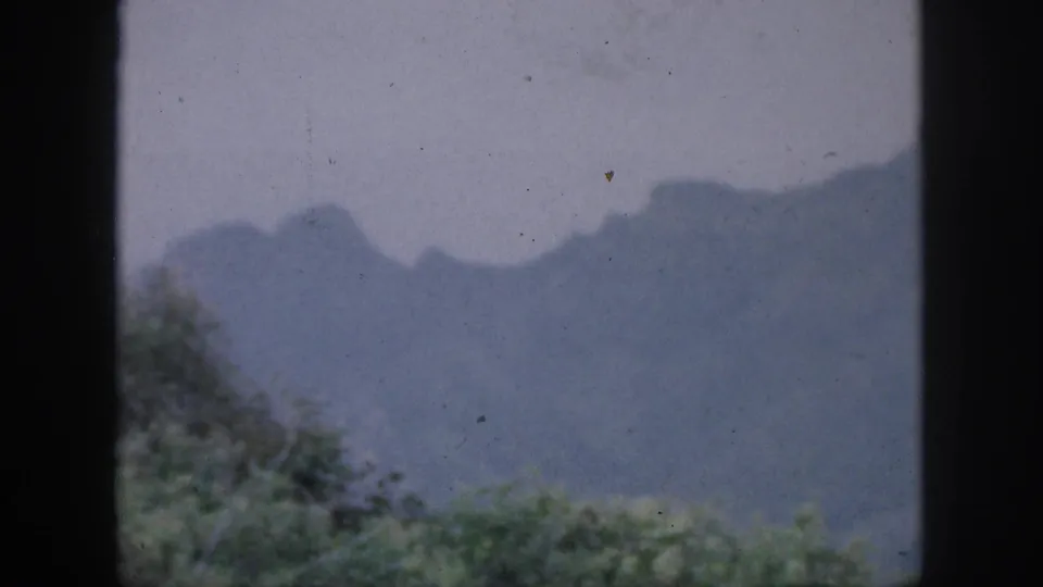1959 Hawaii home-movie view of distant mountain silhouettes and foreground greenery through a vertical window frame.