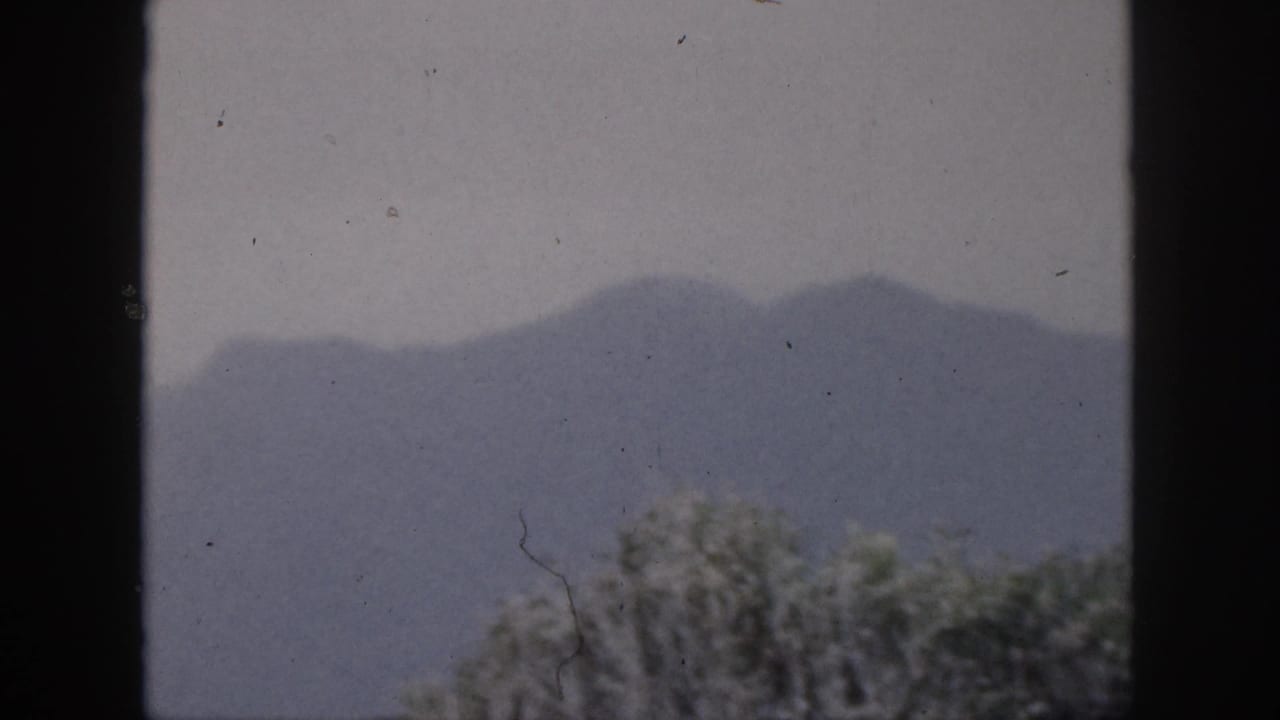 Fog-softened mountains with tree tops below and dark window framing.