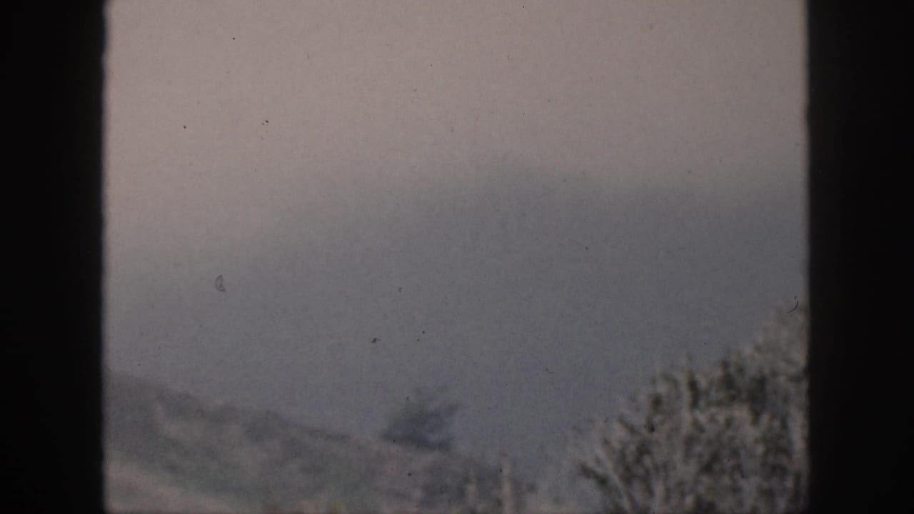 1959 Hawaii home-movie frame showing a soft distant mountain ridge through dark vertical and horizontal window bars.