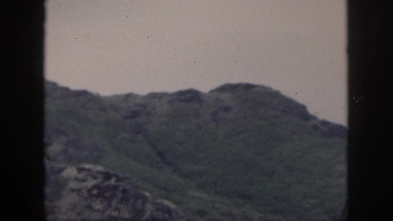 1959 Hawaii 8mm frame with rolling green mountain ridges under a pale sky and dark window edges.