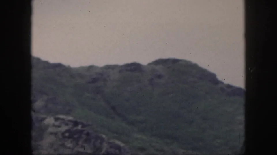 1959 Hawaii 8mm frame with rolling green mountain ridges under a pale sky and dark window edges.