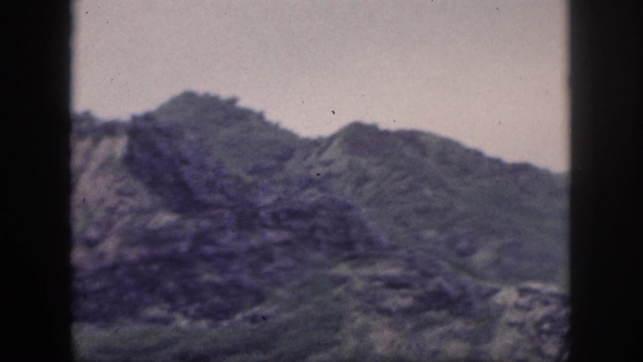 1959 Hawaii home-movie frame showing a rugged, green-streaked mountain ridge beneath a muted sky.