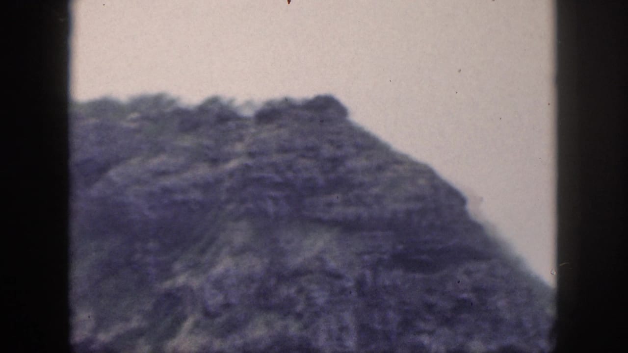 1959 Hawaii landscape frame showing a rounded rocky high point, green vegetation, and purple-blue 8mm color fading.