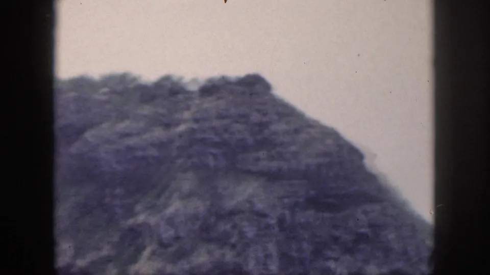 1959 Hawaii landscape frame showing a rounded rocky high point, green vegetation, and purple-blue 8mm color fading.
