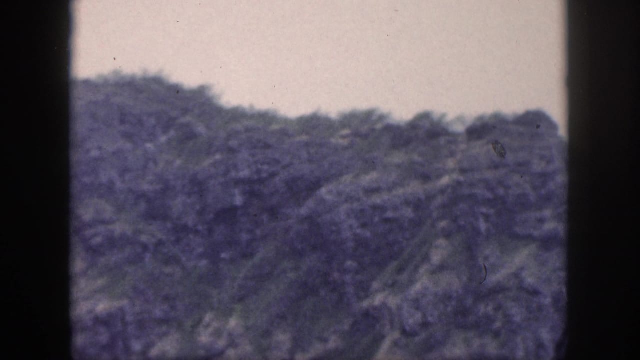 1959 Hawaii 8mm frame showing a distant vegetated mountain ridge with rocky slopes and soft, faded color.