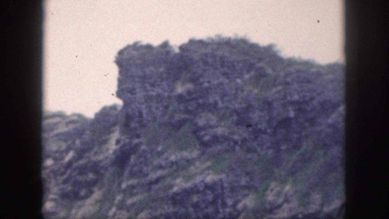 Rocky mountain outcrop with green vegetation seen through dark frame edges.