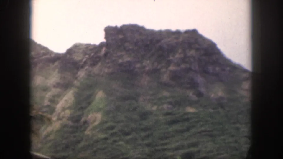 1959 Hawaii 8mm frame showing a steep vegetated slope and dark rocky ridge, with soft focus and faded color.