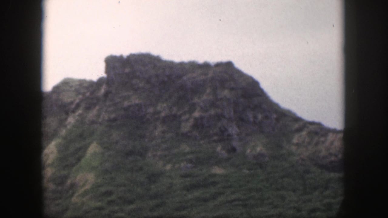 1959 Hawaii 8mm frame showing a rugged green mountain slope viewed through dark window or vehicle framing.