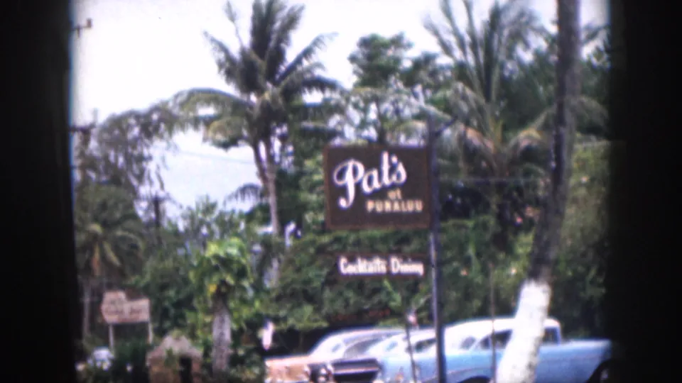 1959 Hawaii roadside scene showing the Pat's at Punaluu sign, palm trees, vegetation, and older parked cars.