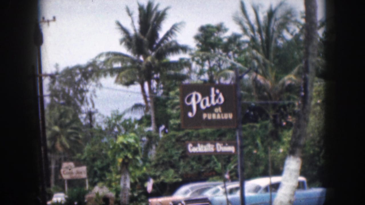 1959 Hawaii 8mm frame of the Pat's at Punaluu roadside sign with palms, tropical greenery, and parked mid-century cars.