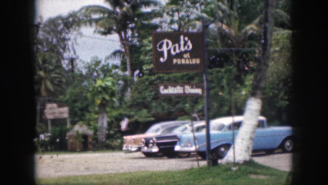 1959 Hawaii home-movie frame showing Pat's at Punalu'u signage, parked classic cars, palms, and roadside greenery.