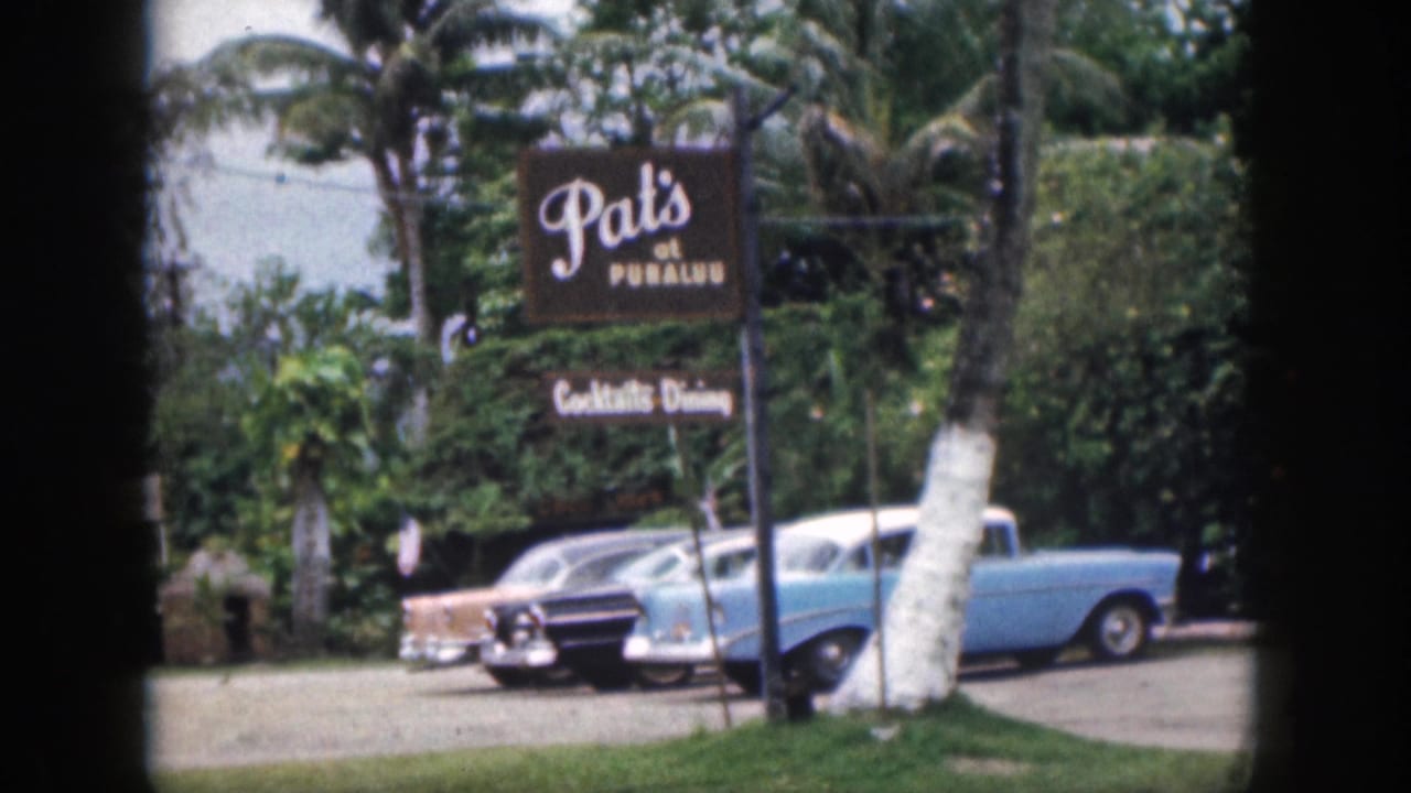 1959 Hawaii frame with Pat's at Punalu'u sign, classic cars, palm trunks, and tropical vegetation along the roadside.