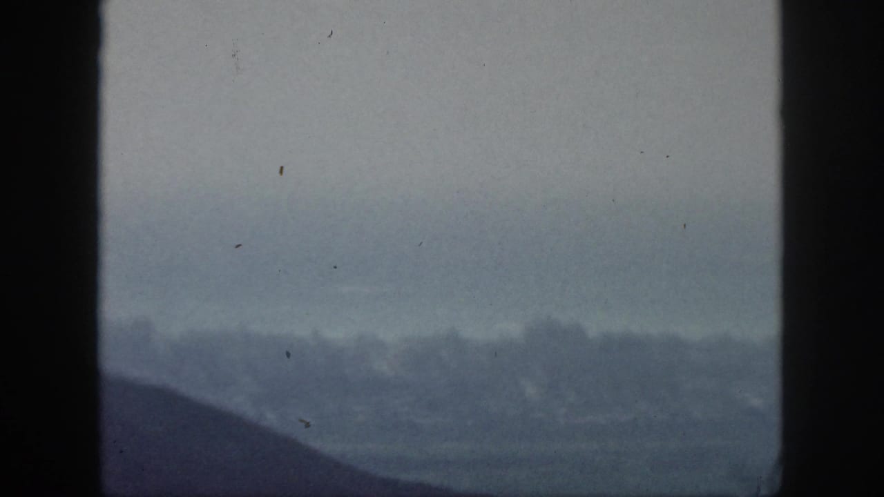 1959 Hawaii 8mm frame with dark foreground framing over a soft, hazy lowland and distant ridgeline.
