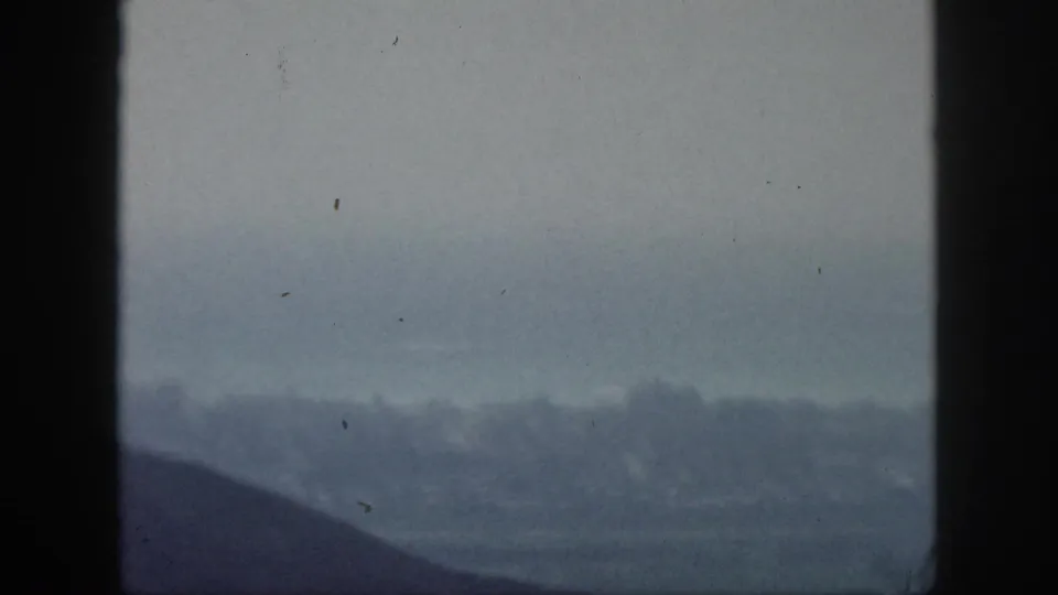 1959 Hawaii 8mm frame with dark foreground framing over a soft, hazy lowland and distant ridgeline.