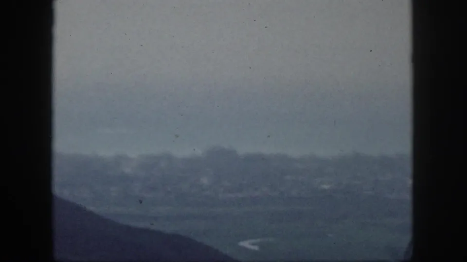 1959 Hawaii 8mm overlook toward a hazy distant settlement or shoreline beneath dark vertical framing.
