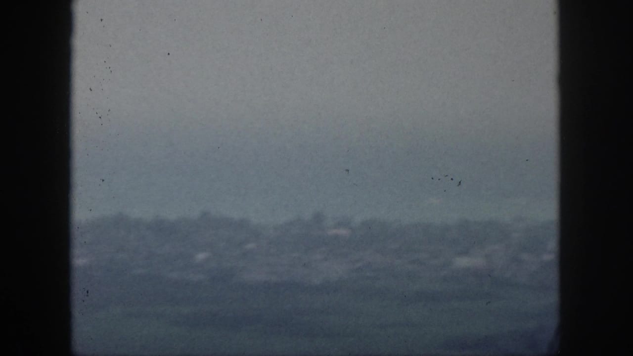 The 8mm frame shows a subdued Hawaii shoreline or city edge seen through a window, with haze softening the background.