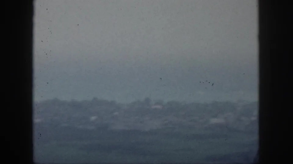 The 8mm frame shows a subdued Hawaii shoreline or city edge seen through a window, with haze softening the background.