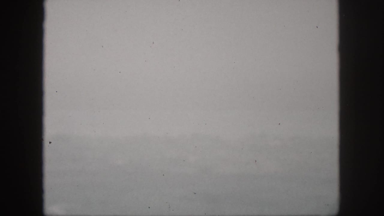 1959 Hawaii home-movie frame showing a gray, fog-softened hillside view through dark vertical window bars.