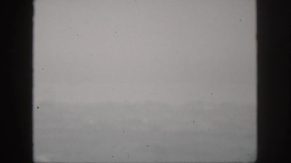 1959 Hawaii home-movie frame showing a gray, fog-softened hillside view through dark vertical window bars.