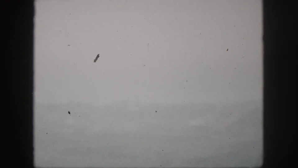A soft 8mm view of mist and faint hills in Hawaii, framed by a dark central window divider.