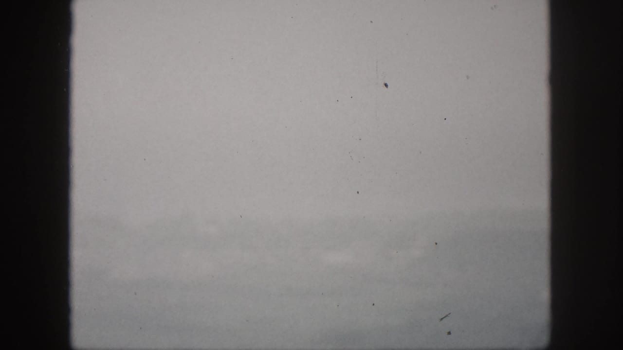 1959 Hawaii 8mm frame with muted gray fog, distant hillside shapes, and dark window framing.