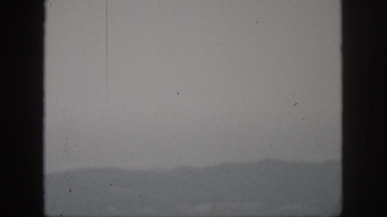 1959 8mm Hawaii landscape frame with a faint hill ridge, heavy haze, and dark window edges.