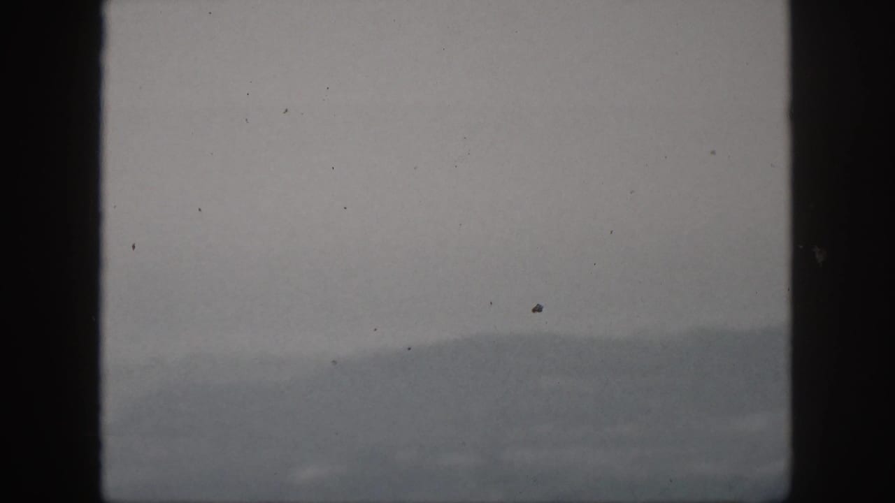 Foggy 1959 Hawaii hill view on 8mm film, framed by dark window bars with dust specks visible.