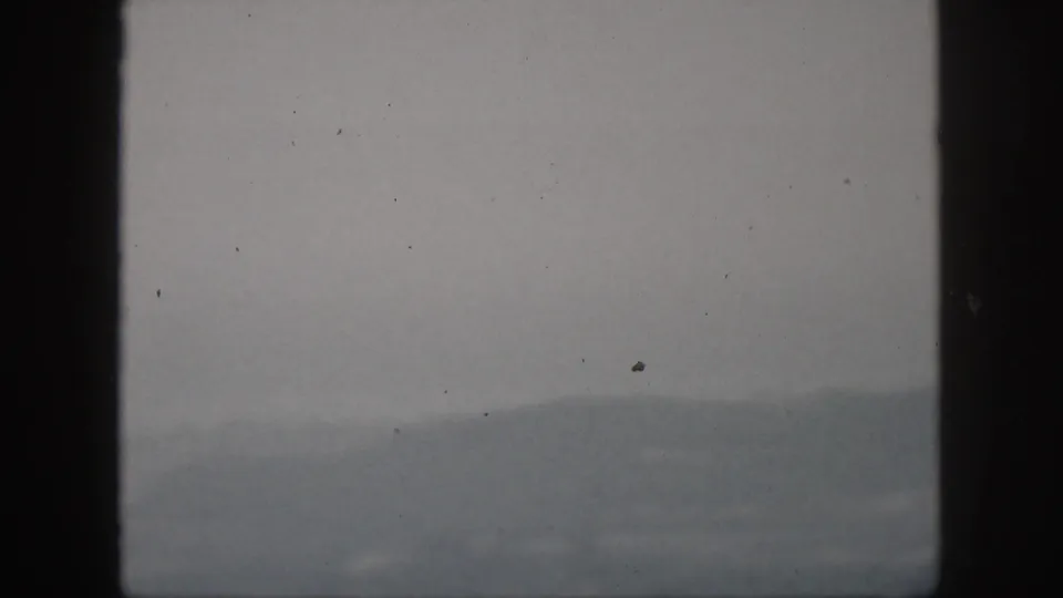 Foggy 1959 Hawaii hill view on 8mm film, framed by dark window bars with dust specks visible.