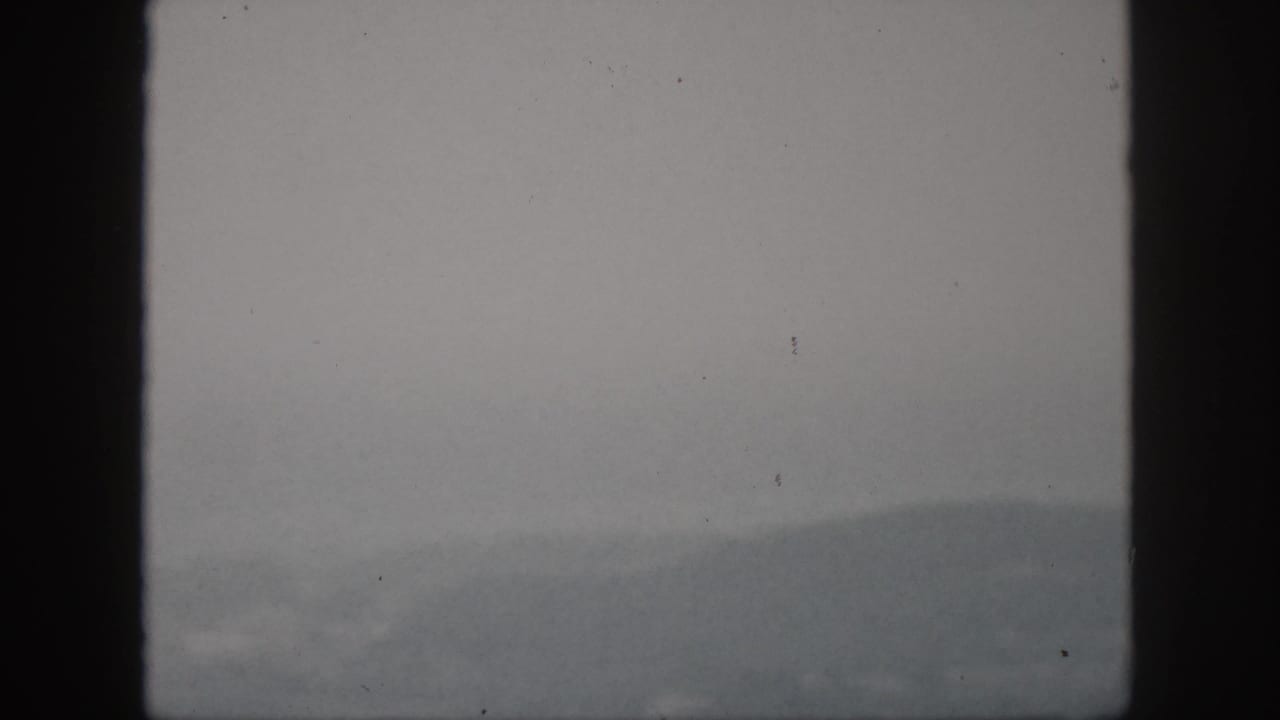 1959 Hawaii home-movie frame showing a hazy mountain ridge through dark window or viewfinder edges under overcast light.
