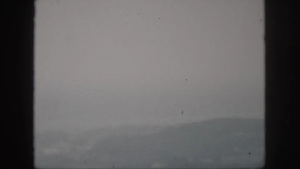 1959 Hawaii home-movie frame showing a hazy mountain ridge through dark window or viewfinder edges under overcast light.