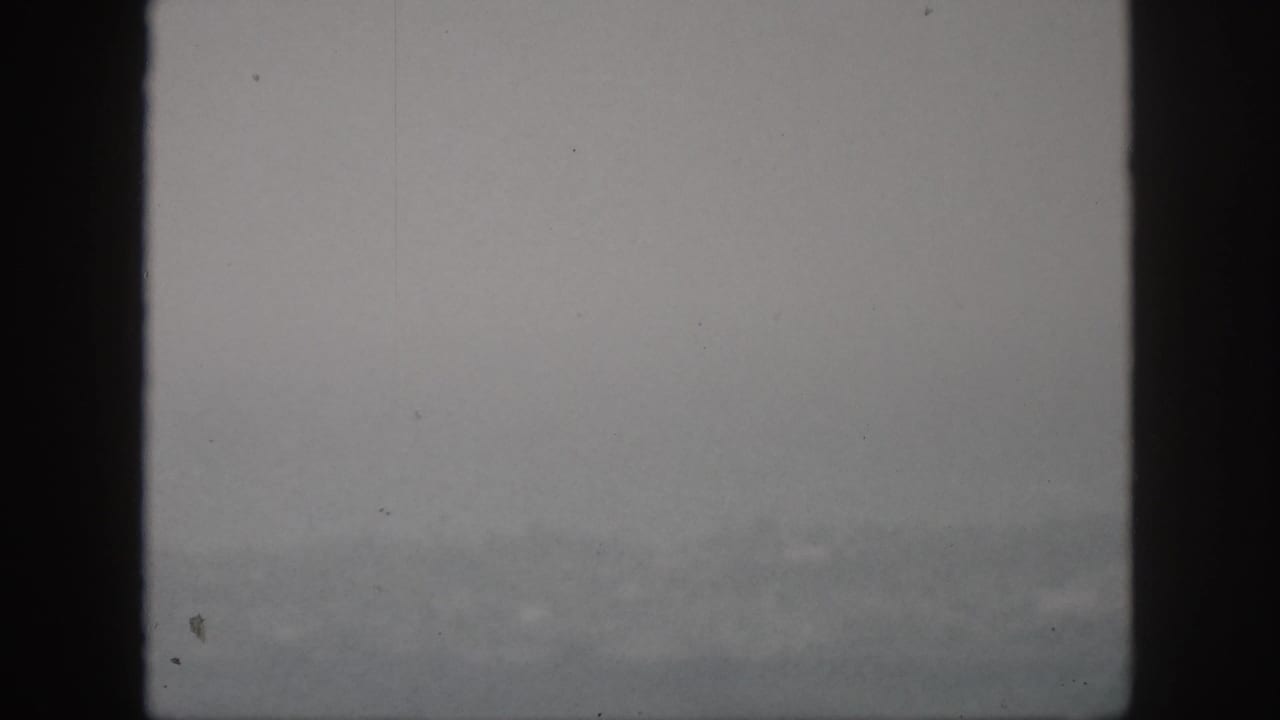 1959 Hawaii 8mm frame showing a pale foggy landscape with faint mountain forms and visible film dust.
