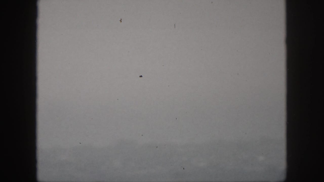 1959 Hawaii home-movie frame with a faint mountain ridge, gray overcast sky, and dark viewfinder-like edges.
